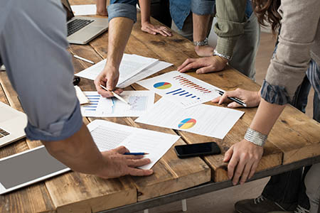 Team members studying charts laid out on a wooden desk.